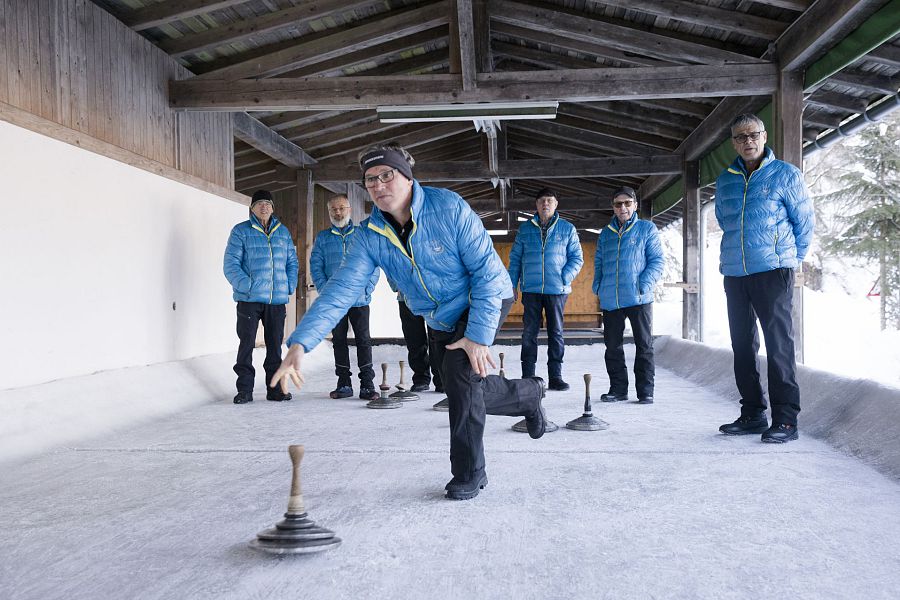Die Eisschützen tragen alle ihre hellblauen warmen Wintersportjacken mit dem Emblem des Eis- und Stockschützenvereins darauf.