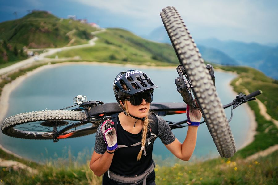 Kitzbüheler Alpen Hero Bike Lena Koller schultert ihr Mountainbike im Hintergrund ein Speichersee am Pengelstein c Daniel Gollner